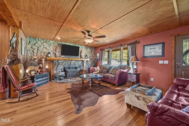 living area with wood ceiling, a ceiling fan, hardwood / wood-style floors, and a wood stove