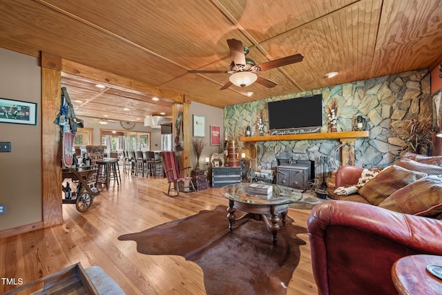 living area featuring wood ceiling, a ceiling fan, wood finished floors, and a stone fireplace
