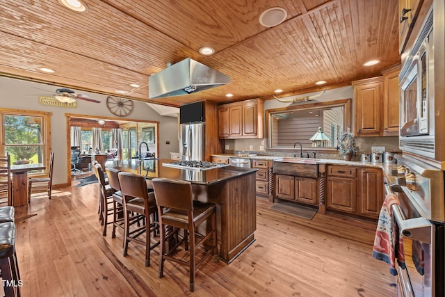 kitchen with wood ceiling, an island with sink, appliances with stainless steel finishes, a kitchen bar, and light wood-style flooring