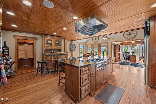 kitchen featuring appliances with stainless steel finishes, wood ceiling, exhaust hood, dark countertops, and a center island with sink