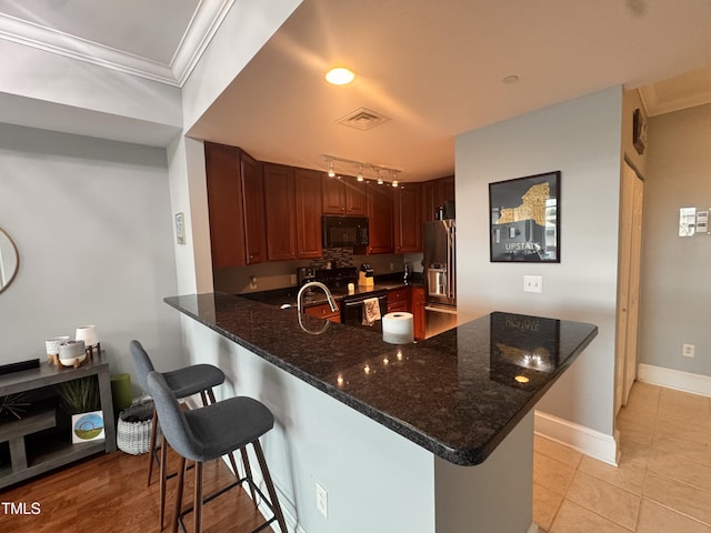 510 Glenwood Ave Unit 606, Raleigh, NC 27603 - kitchen with black appliances, a peninsula, crown molding, a breakfast bar area, and dark stone counters