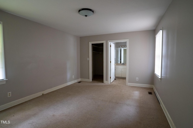 2100 Breeze Rd, Raleigh, NC 27608 - unfurnished bedroom featuring light colored carpet, ensuite bathroom, a closet, and a walk in closet
