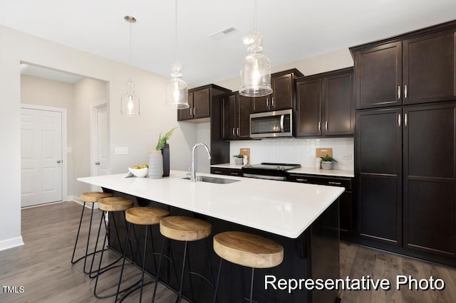 59 Curling Creek Dr Unit I285, Clayton, NC 27527 - kitchen featuring stainless steel microwave, dark wood-style floors, a breakfast bar, stove, and a kitchen island with sink