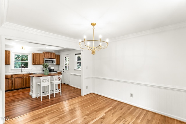 212 Heidinger Dr, Cary, NC 27511 - kitchen featuring appliances with stainless steel finishes, brown cabinetry, light wood-style floors, a chandelier, and a breakfast bar