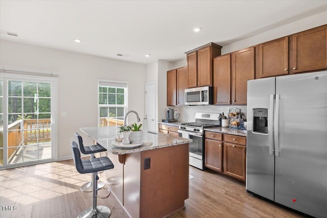 6620 Pathfinder Way, Raleigh, NC 27616 - kitchen with appliances with stainless steel finishes, an island with sink, light stone counters, brown cabinets, and a breakfast bar