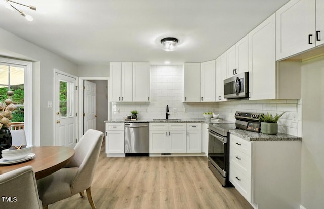 117 S Woodstone Dr, Archer Lodge, NC 27527 - kitchen featuring appliances with stainless steel finishes, tasteful backsplash, light stone countertops, white cabinetry, and light wood-style flooring