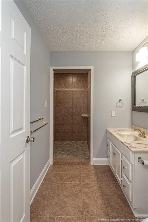2408 Crabtree Ct, Fayetteville, NC 28304 - bathroom with vanity, tiled shower, a textured ceiling, and tile patterned floors