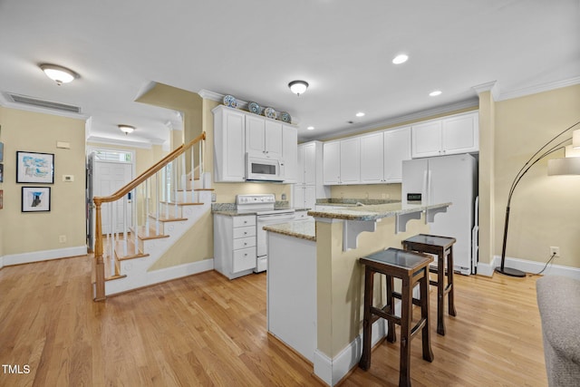 717 Mcclure Dr, Raleigh, NC 27603 - kitchen featuring white appliances, crown molding, a breakfast bar area, white cabinetry, and light wood finished floors