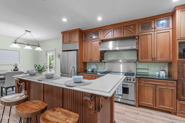 1408 Old Ivey Rd, Apex, NC 27523 - kitchen with stainless steel appliances, wall chimney exhaust hood, brown cabinetry, light wood-style floors, and a center island with sink