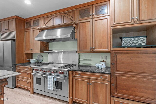 1408 Old Ivey Rd, Apex, NC 27523 - kitchen with high quality appliances, ventilation hood, brown cabinetry, dark stone countertops, and glass insert cabinets