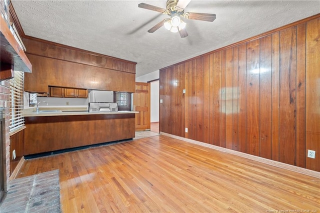 395 N Gaines St, Southern Pines, NC 28387 - kitchen featuring brown cabinets, light wood-style flooring, a textured ceiling, wooden walls, and ceiling fan