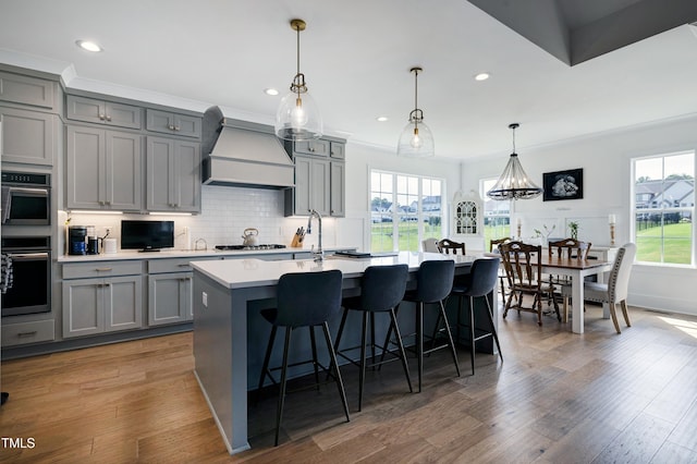447 Marcellus Way, Clayton, NC 27527 - kitchen featuring premium range hood, gray cabinets, light countertops, a kitchen island with sink, and a kitchen breakfast bar