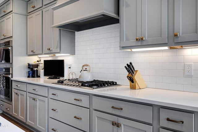 447 Marcellus Way, Clayton, NC 27527 - kitchen featuring gray cabinets, custom exhaust hood, stainless steel gas stovetop, light countertops, and backsplash