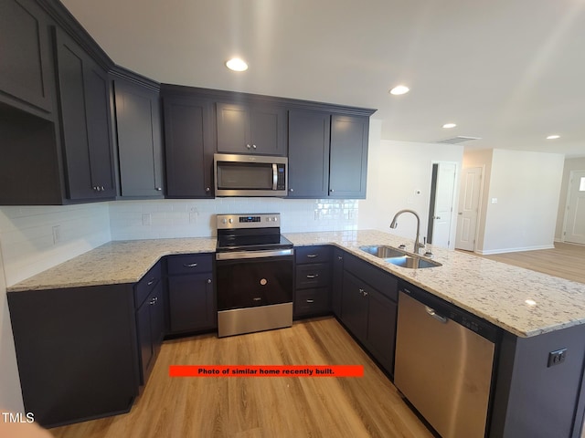 307 E Holmes St, Benson, NC 27504 - kitchen featuring appliances with stainless steel finishes, a peninsula, light wood-style flooring, light stone countertops, and backsplash