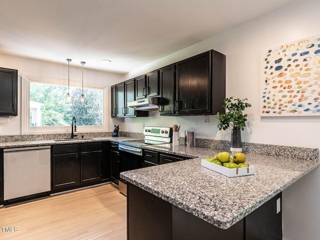 3205 Dell Dr, Raleigh, NC 27609 - kitchen featuring appliances with stainless steel finishes, a peninsula, dark cabinetry, under cabinet range hood, and light stone counters