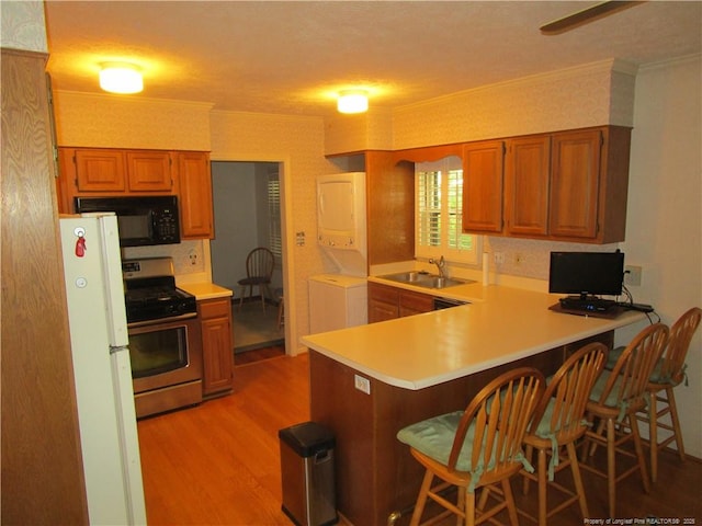 432 Rollingwood Cir, Fayetteville, NC 28305 - kitchen featuring black microwave, gas stove, stacked washer and clothes dryer, freestanding refrigerator, and light wood-type flooring