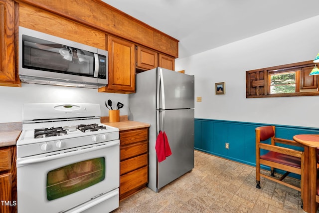 4134 King Charles Rd, Durham, NC 27707 - kitchen with appliances with stainless steel finishes, brown cabinets, light countertops, and a wainscoted wall