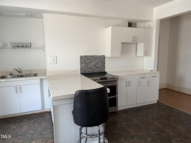 903 New Bern Ave, Raleigh, NC 27601 - kitchen featuring double oven range, tile counters, white cabinetry, a peninsula, and a breakfast bar area
