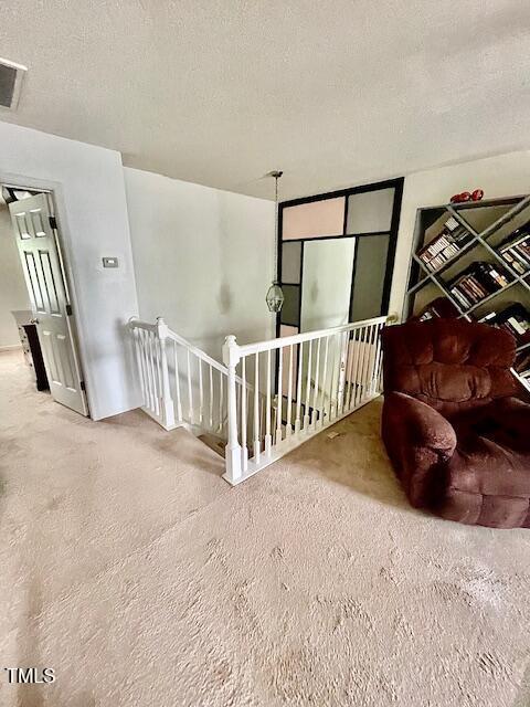 6328 Bermuda Way, Whitsett, NC 27377 - living area featuring an upstairs landing, carpet floors, and a textured ceiling