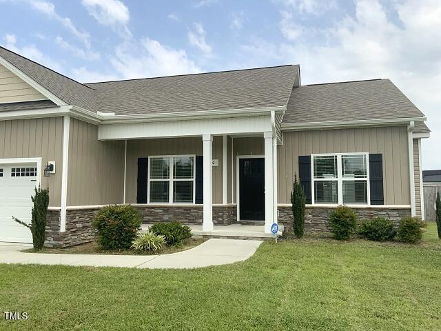 101 Mutton Dr, Pikeville, NC 27863 - view of front of house with an attached garage, stone siding, a front yard, a porch, and roof with shingles