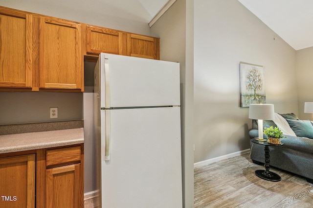 3050 Trailwood Pines Ln Unit 303, Raleigh, NC 27603 - kitchen featuring freestanding refrigerator, vaulted ceiling, light wood-style floors, brown cabinetry, and light countertops