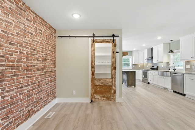 7722 NC-27, Lillington, NC 27546 - kitchen featuring stainless steel appliances, a barn door, wall chimney exhaust hood, light wood-style floors, and white cabinetry