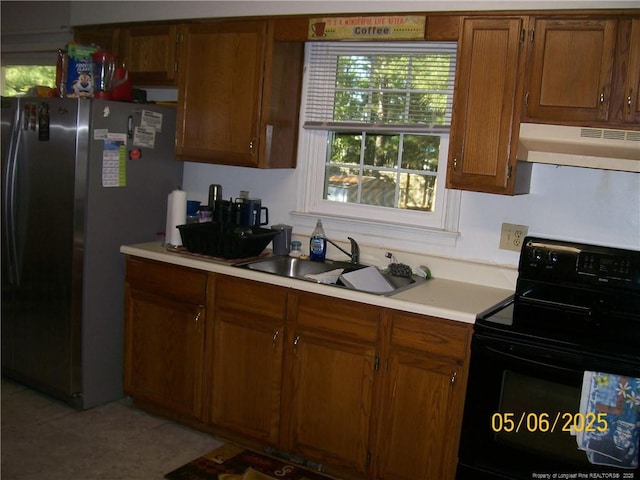 5212 Delco St, Fayetteville, NC 28311 - kitchen with black electric range, under cabinet range hood, freestanding refrigerator, light countertops, and brown cabinets
