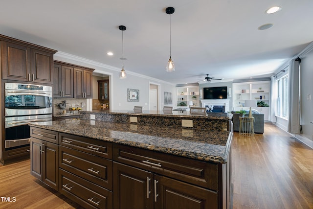 1013 Shasta Daisy Dr, Wake Forest, NC 27587 - kitchen featuring double oven, a ceiling fan, a center island, ornamental molding, and a fireplace