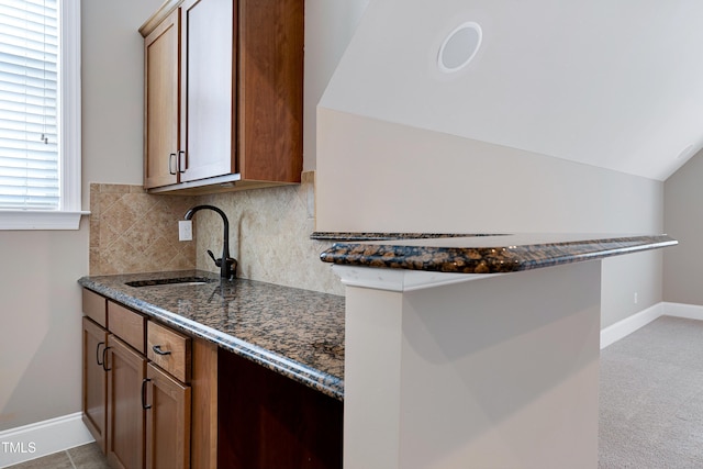 1013 Shasta Daisy Dr, Wake Forest, NC 27587 - kitchen with dark stone countertops, decorative backsplash, brown cabinetry, lofted ceiling, and light colored carpet