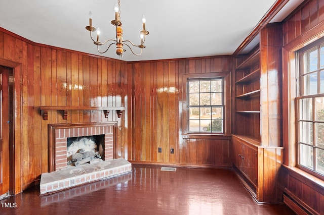 221 Whitfield St, Enfield, NC 27823 - unfurnished living room featuring wood walls, a chandelier, plenty of natural light, and a brick fireplace