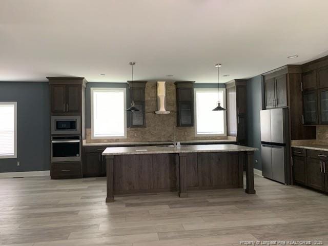 1484 Brayboy Rd, Rowland, NC 28383 - kitchen featuring stainless steel appliances, wall chimney range hood, decorative backsplash, light wood-style floors, and a center island with sink