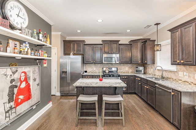 2407 Cattail Pond Dr, Zebulon, NC 27597 - kitchen with appliances with stainless steel finishes, dark brown cabinetry, dark wood-style floors, a kitchen island, and ornamental molding