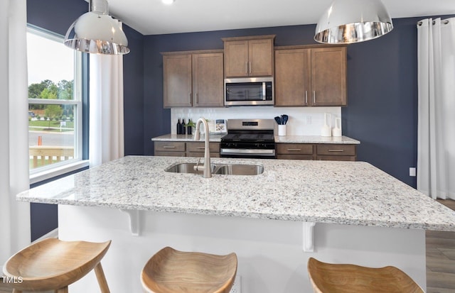 1516 Tamarisk Ln, Durham, NC 27703 - kitchen with appliances with stainless steel finishes, light stone counters, a kitchen island with sink, and a kitchen bar