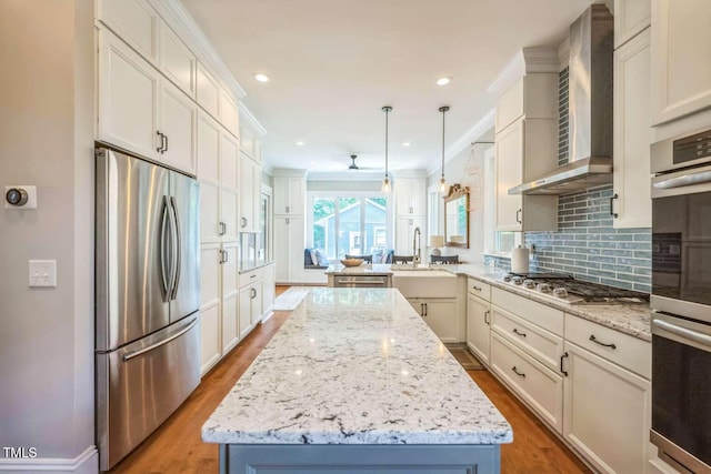 1213 Pierce St, Raleigh, NC 27605 - kitchen with stainless steel appliances, wall chimney range hood, a kitchen island, wood finished floors, and ornamental molding