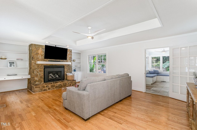 6025 Tarnhour Ct, Raleigh, NC 27612 - living area with a ceiling fan, a tray ceiling, light wood-type flooring, and a stone fireplace