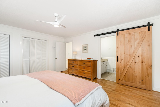 6025 Tarnhour Ct, Raleigh, NC 27612 - bedroom featuring a barn door, light wood-style floors, connected bathroom, a ceiling fan, and two closets