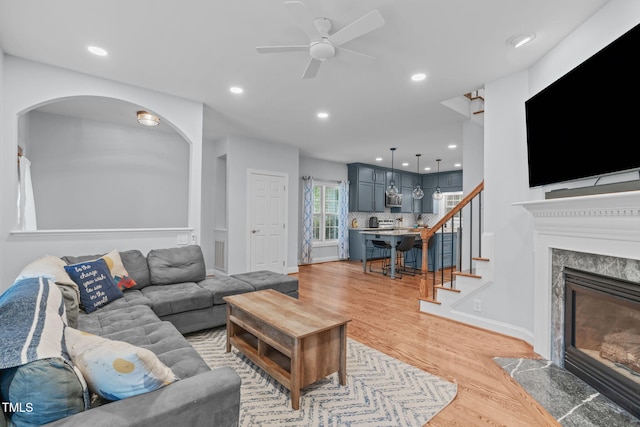 511 Scotts Ridge Trl, Apex, NC 27502 - living room featuring light wood-type flooring, a ceiling fan, a fireplace, arched walkways, and stairs
