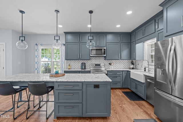 511 Scotts Ridge Trl, Apex, NC 27502 - kitchen featuring appliances with stainless steel finishes, a center island, backsplash, light stone counters, and light wood-style flooring