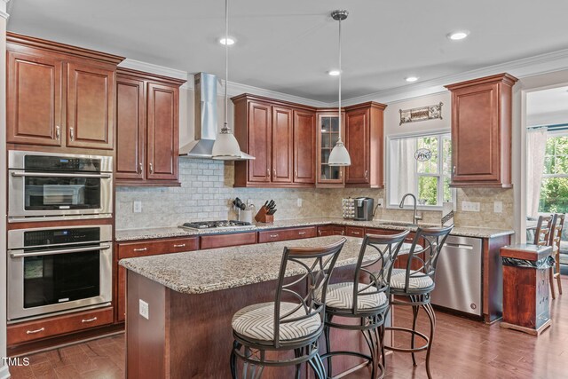 1950 Firenza Dr, Apex, NC 27502 - kitchen featuring stainless steel appliances, wall chimney exhaust hood, decorative columns, pendant lighting, and glass insert cabinets
