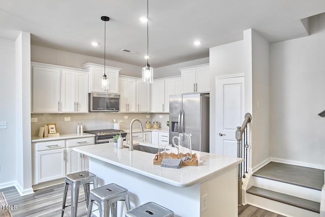 1004 Citadel Ave, Durham, NC 27713 - kitchen with stainless steel appliances, light wood-type flooring, white cabinets, a kitchen island with sink, and recessed lighting