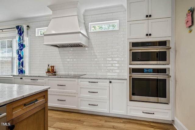 309 N Mason St, Apex, NC 27502 - kitchen featuring premium range hood, black electric stovetop, stainless steel double oven, backsplash, and white cabinetry