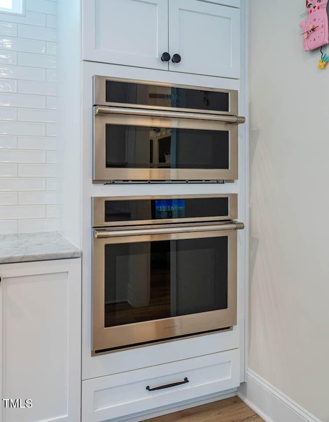 309 N Mason St, Apex, NC 27502 - kitchen view of stainless steel double oven, light stone countertops, white cabinets, and wood finished floors