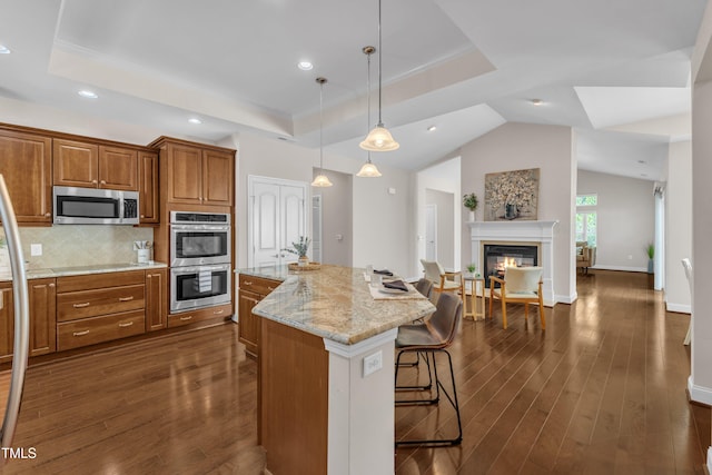 936 Blue Bird Ln, Wake Forest, NC 27587 - kitchen featuring appliances with stainless steel finishes, brown cabinets, light stone counters, a kitchen breakfast bar, and dark wood finished floors