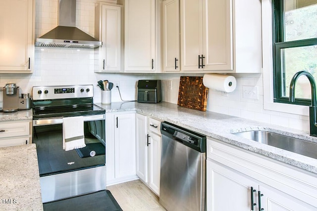 1523 Ivy Ln, Raleigh, NC 27609 - kitchen with wall chimney range hood, appliances with stainless steel finishes, tasteful backsplash, light stone counters, and white cabinetry