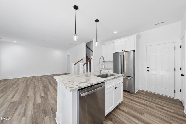 1254 Camden Ave, Durham, NC 27701 - kitchen featuring appliances with stainless steel finishes, light wood finished floors, white cabinetry, light stone countertops, and a kitchen island with sink