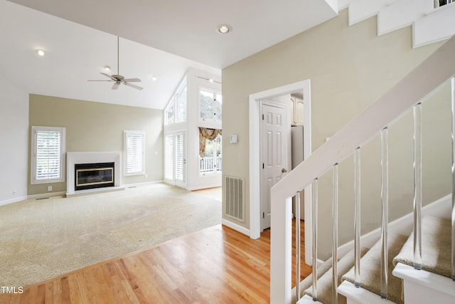 2944 Ballybunion Way, Raleigh, NC 27613 - unfurnished living room featuring light wood-type flooring, stairs, high vaulted ceiling, a glass covered fireplace, and a ceiling fan