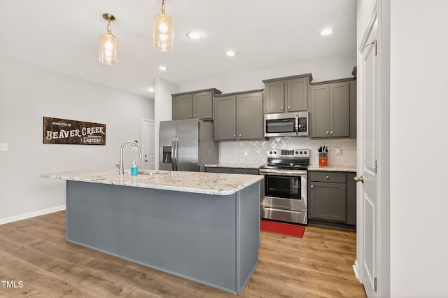 611 Laurel Lake Rd, Salemburg, NC 28385 - kitchen featuring stainless steel appliances, gray cabinetry, backsplash, an island with sink, and light stone countertops