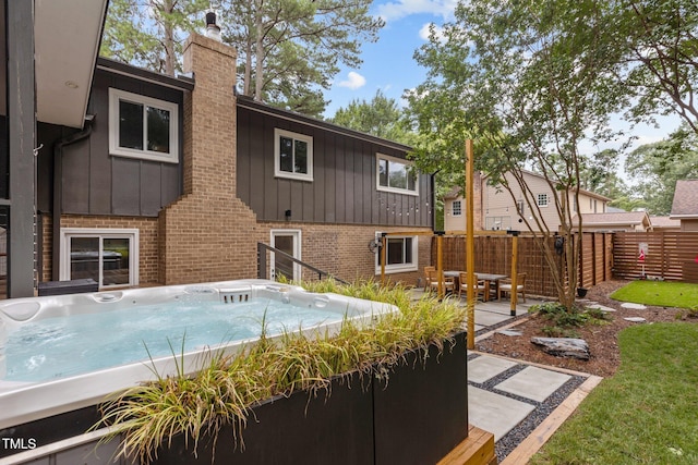 3033 Sylvania Dr, Raleigh, NC 27607 - rear view of house featuring board and batten siding, a hot tub, brick siding, a chimney, and a patio