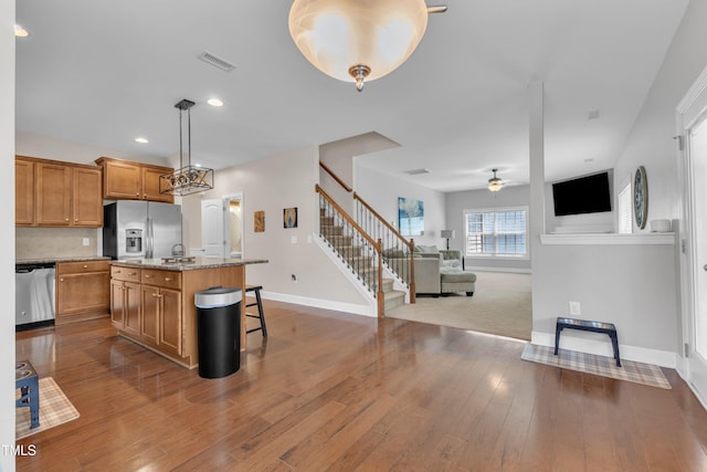 2700 Banks Lake Ct, Fuquay Varina, NC 27526 - kitchen with stainless steel appliances, brown cabinets, open floor plan, ceiling fan, and a kitchen breakfast bar