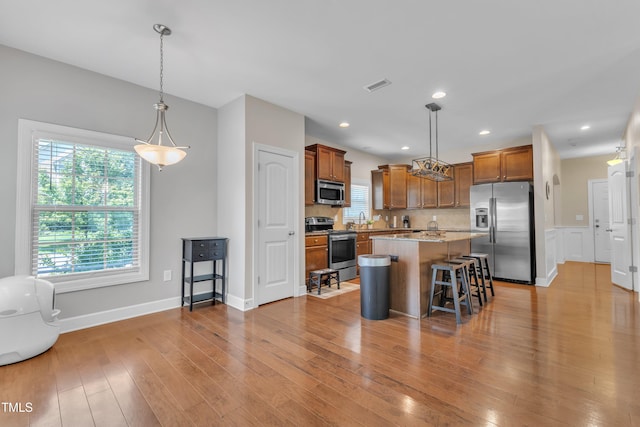 2700 Banks Lake Ct, Fuquay Varina, NC 27526 - kitchen featuring appliances with stainless steel finishes, light wood-style floors, a breakfast bar area, brown cabinetry, and hanging light fixtures